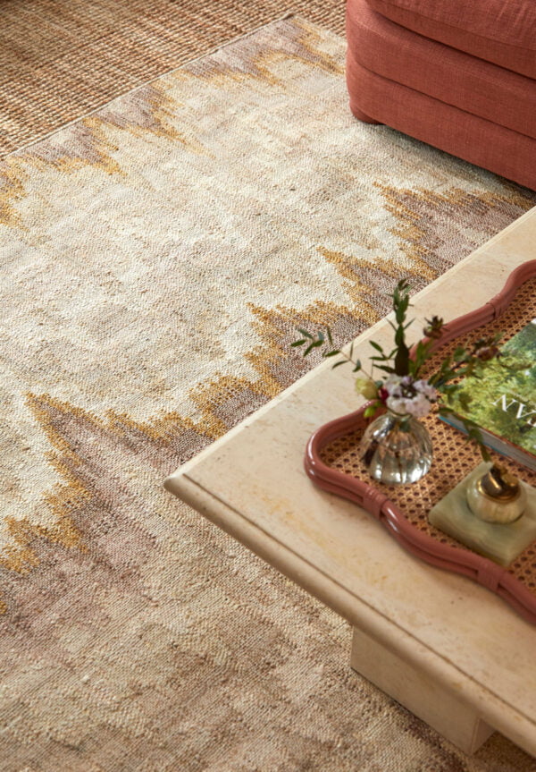 The corner of a coffee table with a brick-coloured rattan tray on it and a bespoke neutral-coloured rug on the floor.